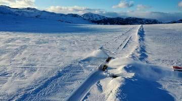 Dronebilde av brøyting på Valdresflya der det brøytes gjennom meterhøy snø